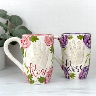 Two coffee mugs decorated with purple and pink florals with two children's handprints