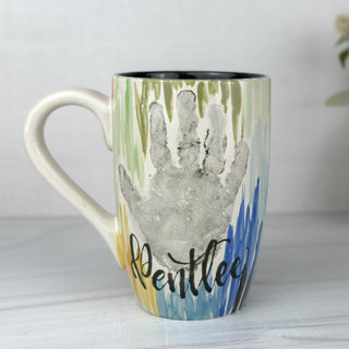 Coffee mug decorated with colorful line art and a child's handprint 