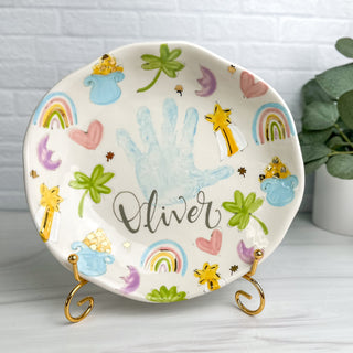 Plate on a gold stand decorated with lucky charms themed art, made with a child's handprint.