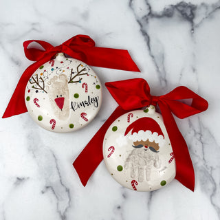 Round ornament decorated with Santa made from a child's handprint and a reindeer made from a child's footprint