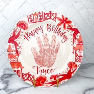 Circular "Happy Birthday" plate decorated with red chinoiserie artwork and a child's handprint. 