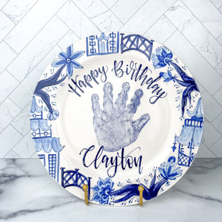 Circular "Happy Birthday" plate decorated with blue chinoiserie artwork and a child's handprint. 