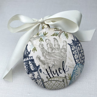 Circular ornament decorated with chinoiserie artwork and a child's handprint. 