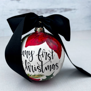 Round ornament decorated with "My First Christmas" and poinsettias. 