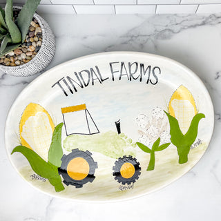Round platter decorated with a green tractor and two corn stalks, all made with three children's footprints.