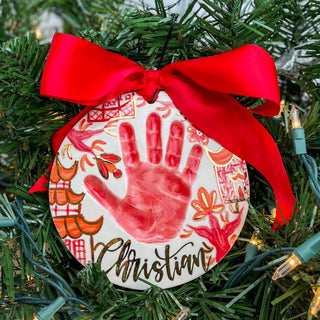 Circular ornament decorated with red chinoiserie artwork and a child's handprint. 