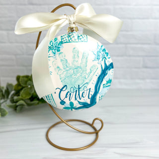 Circular ornament decorated with chinoiserie artwork and a child's handprint. 