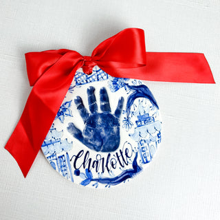 Circular ornament decorated with blue chinoiserie artwork and a child's handprint. 