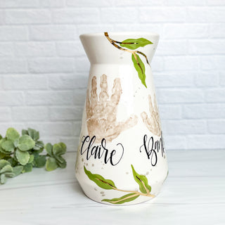 Large vase decorated with greenery and made with two children's handprints.