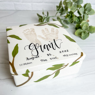 Box decorated with greenery and made with a child's hand and footprint. Also includes child's birth information (weight, time of birth, length)