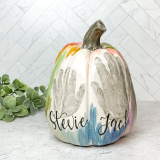 Pumpkin decorated with colorful line art and two children's handprints 